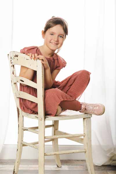 Erstklässlerin sitzt auf einem alten Stuhl und lächelt in die Kamera