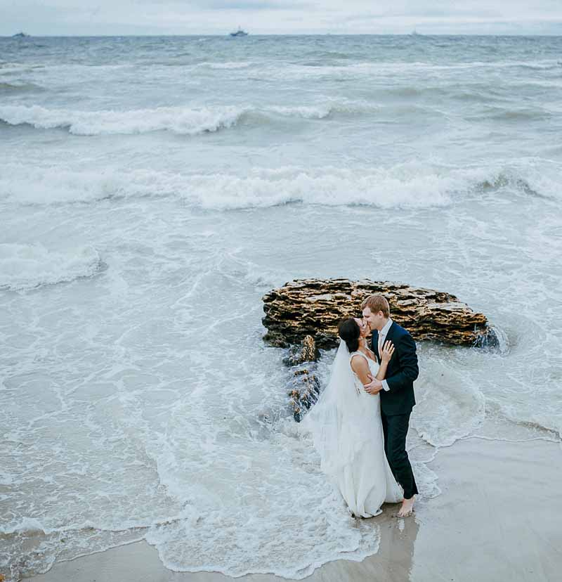 Brautpaar steht am Strand in den Wellen.