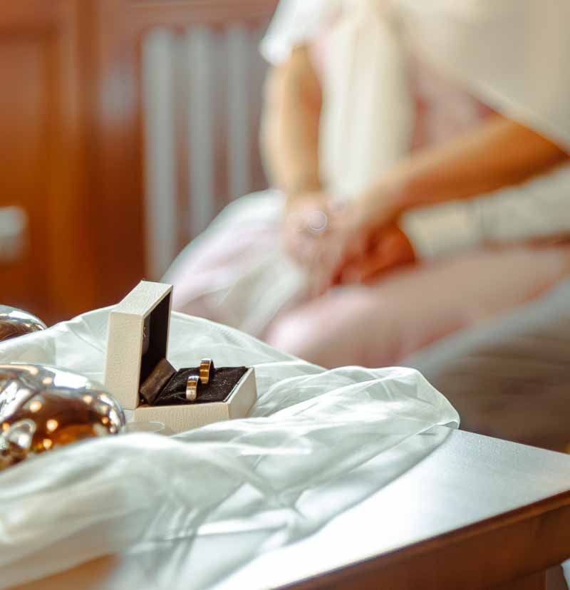 Hochzeitsreportage: Die Ringe in der Schatulle sind zu sehen. Dahinter unscharf, das Brautpaar das sich an den Händen hält.